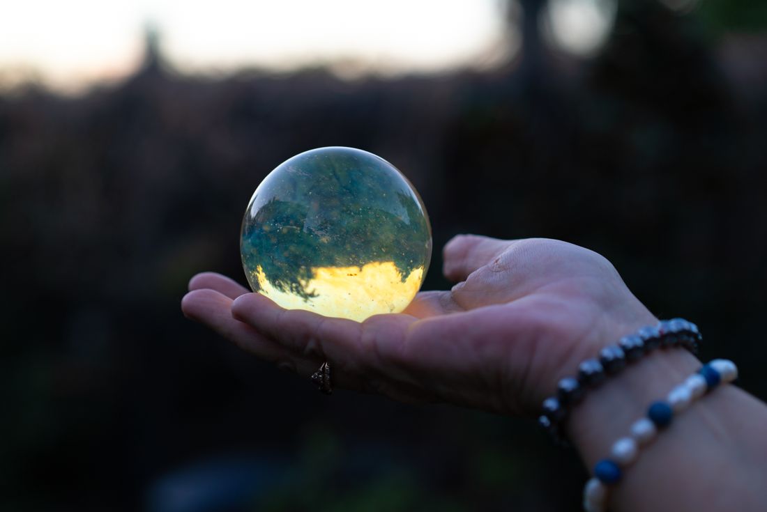 A hand holding a glowing crystal ball at dusk